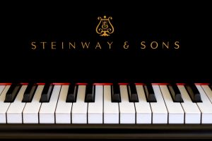 Steinway & Sons logo close up. Classic gold lettering above the piano keys of a ebony black Steinway grand piano