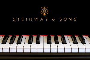 Steinway & Sons logo close up. Classic gold lettering above the piano keys of a ebony black Steinway grand piano